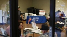 In this Feb. 8, 2020, photo, people volunteer to get people registered to vote and a booth offering employment for the upcoming 2020 census stands in the background, during the celebration of the town's 45th year since it was incorporated, in Guadalupe, A