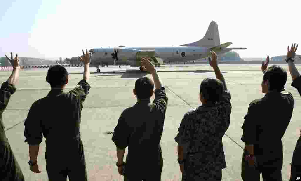 Para anggota awak melambaikan tangan pada pesawat patroli Pertahanan Maritim Jepang P3C Orion saat meninggalkan pangkalan angkatan udara Malaysia di Subang menuju Australia untuk bergabung dalam operasi pencarian pesawat Malaysia Airlines yang hilang (23/3). (AP/Lai Seng Sin)