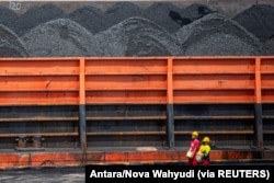 Pekerja berjalan di dekat kapal tunda yang membawa tongkang batu bara di pelabuhan di Palembang, Sumatera Selatan, 4 Januari 2022. (Foto: Antara/Nova Wahyudi via REUTERS)