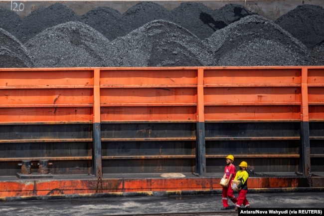 Pekerja berjalan di dekat kapal tunda yang membawa tongkang batu bara di pelabuhan di Palembang, Sumatera Selatan, 4 Januari 2022. (Foto: Antara/Nova Wahyudi via REUTERS)