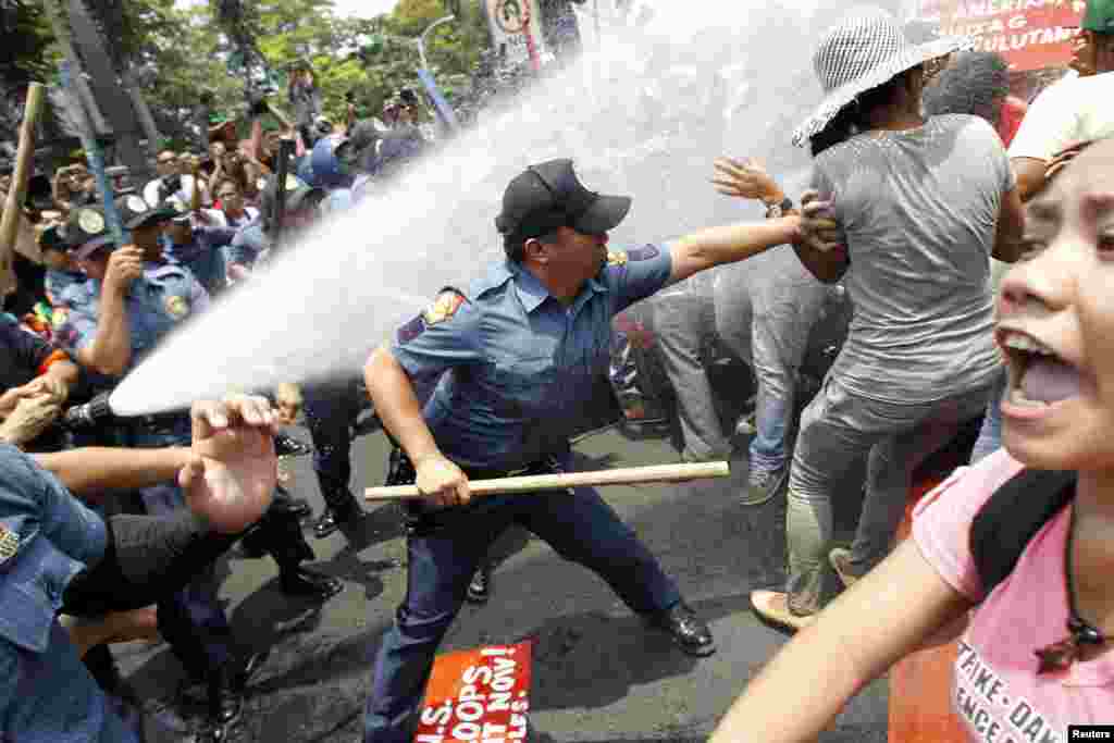 An anti-riot policeman reaches to grab a protester as they are hit with a water cannon during a protest against the upcoming visit of U.S. President Barack Obama next week, in front of the U.S. embassy in Manila, Philippines, April 23, 2014.