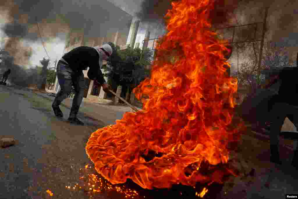 A demonstrator moves a burning tire during an anti-Israel protest following the funeral of Palestinian man Ibraheem Yakoub, in Kifl Haris in the Israeli-occupied West Bank.