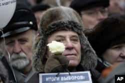 FILE - An elderly protester holds a white flower as symbol of revolution and a paper with the words "election results" during a protest against alleged vote rigging in Russia's parliamentary elections on Sakharov Avenue in Moscow, Dec. 24, 2011.