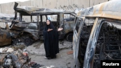 A woman gestures next to vehicles destroyed in a car bomb attack in the Shaoula neighbourhood of Baghdad, Oct. 12, 2014. 