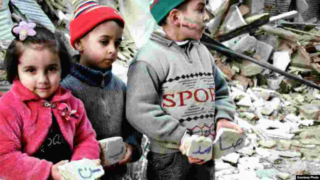 Three Syrian children hold pieces of stone from bombed structure in Homs, January 10, 2013 (Lens Young Homsi)