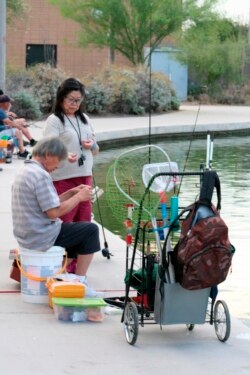 In this April, 30, 2020 photo, a couple sets up their lines to fish at Veterans Oasis Park in Chandler, Ariz. Fishing at community lakes has become a popular outdoor activity for people who have been locked up in their homes during the coronavirus pandemic. Many state fishing have continued to stock lakes during the outbreak. (AP Photo/John Marshall)