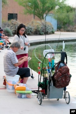 In this April, 30, 2020 photo, a couple sets up their lines to fish at Veterans Oasis Park in Chandler, Ariz. Fishing at community lakes has become a popular outdoor activity for people who have been locked up in their homes during the coronavirus pandemic. Many state fishing have continued to stock lakes during the outbreak. (AP Photo/John Marshall)