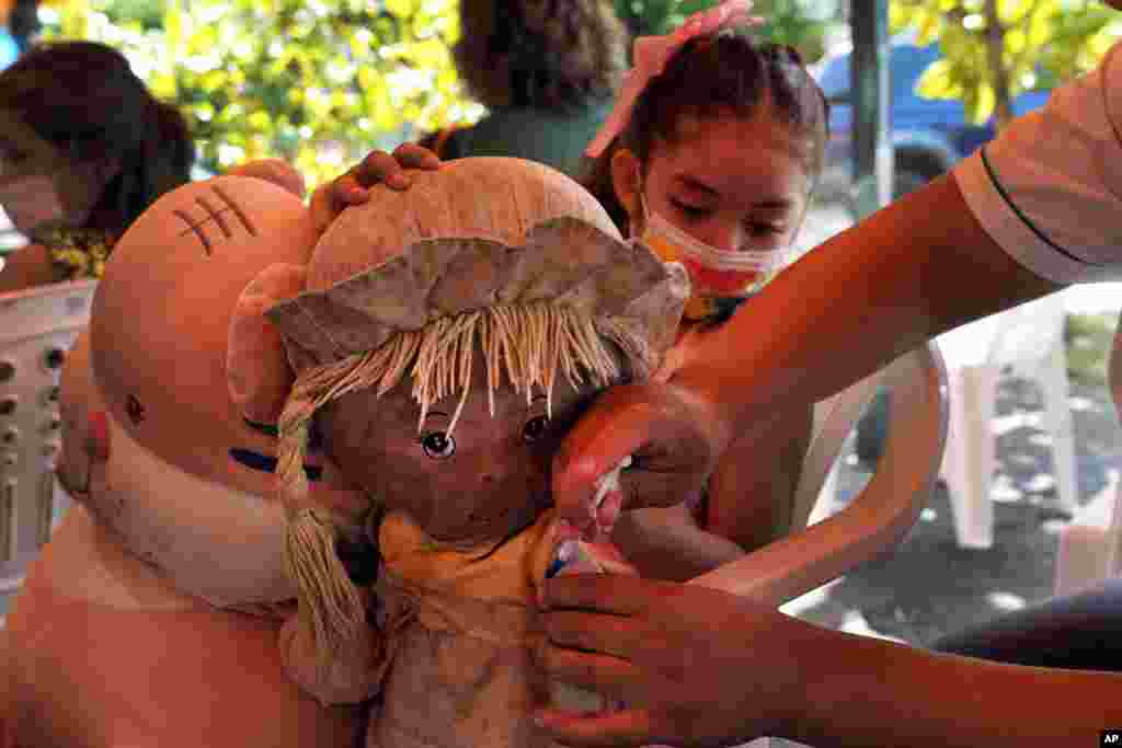 A health worker pretends to give a shot to a girl&#39;s doll to help put her at ease before giving her a shot of COVID-19 vaccine, at a sports center as children start getting vaccinated in Asuncion, Paraguay.