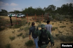 FILE - A U.S. border patrol agent escorts men being detained after entering the United States by crossing the Rio Grande river from Mexico, in Roma, Texas, May 11, 2017.