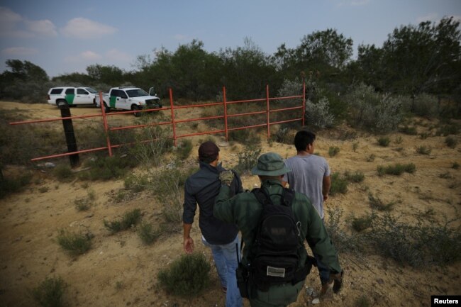 FILE - A U.S. border patrol agent escorts men being detained after entering the United States by crossing the Rio Grande river from Mexico, in Roma, Texas, May 11, 2017.