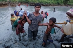 FILE - A Rohingya refugee man helps children through the mud after crossing the Naf River at the Bangladesh-Myanmar border in Palong Khali, near Cox’s Bazar, Bangladesh, Nov. 1, 2017.