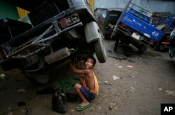 Biswa Gurung, a seven-year-old Indian boy talks to a colleague as he works at an automobile workshop in Gauhati, Oct. 12, 2014.