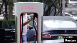 FILE - A man finishes to charge his Tesla car at a charging station in Beijing, China, July 11, 2018. 