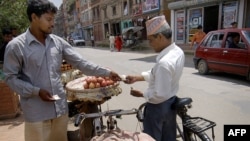 FILE - A vendor (L) exchanges money with a customer as he sells apples off his pushbike on the roadside in Lalitpur, south of Kathmandu, Nepal.