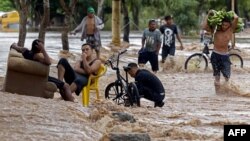 A yougster carries bananas as he wades near men sitting at a flooded street in El Progreso, department of Yoro, Honduras on November 18, 2020, after the passage of Hurricane Iota, now downgraded to Tropical Storm. 