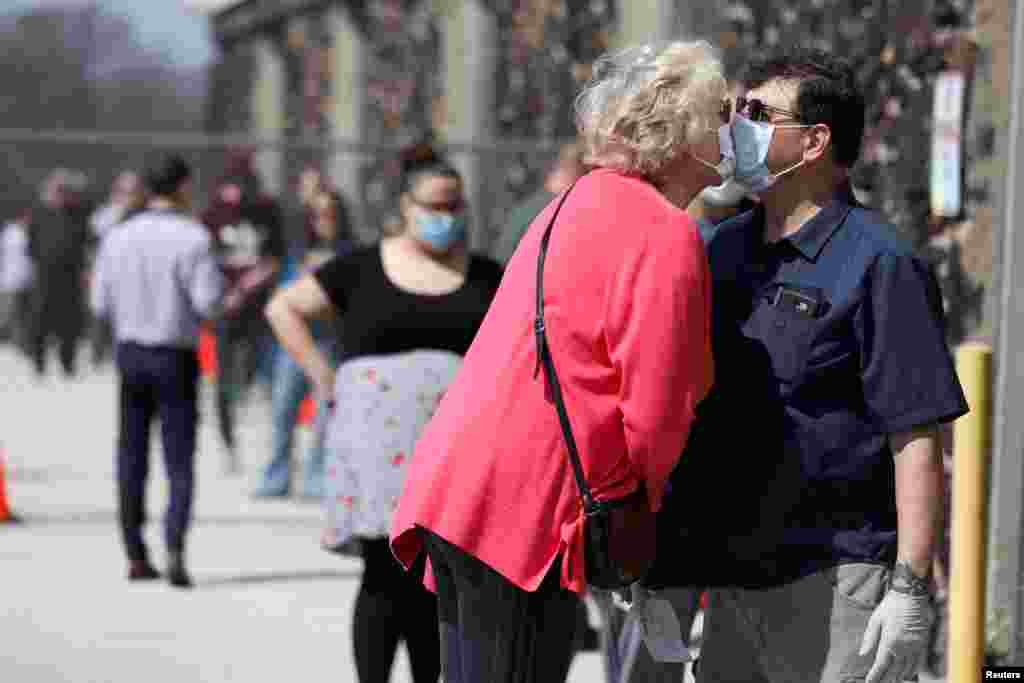 Los votantes Jeff Tragitz, a la derecha, y Lori Walter se besan con máscaras, mientras esperan en la fila frente a un colegio electoral en la Preparatoria Hamilton durante las elecciones primarias presidenciales, celebradas en medio del brote de la enfermedad por coronavirus (COVID-19), en Milwaukee, Wisconsin. EE. UU., el 7 de abril de 2020.