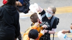 Žena poliva mlekom lice demonstranta koga je policija isprskala suzavcem drugog dana protesta u Mineapolisu.