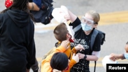 Žena poliva mlekom lice demonstranta koga je policija isprskala suzavcem drugog dana protesta u Mineapolisu.