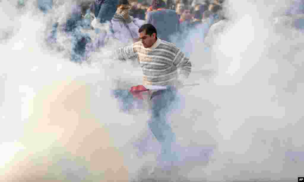 A protester carrying an Egyptian flag runs through clouds of tear gas at a demonstration in Cairo, Jan. 25, 2011.