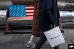 FILE - A couple carries a paper bag containing goods purchased from American brand Champion past a bench painted with the U.S. flag at a Beijing mall, Feb. 13, 2019.