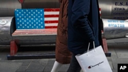A couple carries a paper bag containing goods purchased from American brand Champion past a bench painted with the U.S. flag at the capital city's popular shopping mall in Beijing, Feb. 13, 2019. 