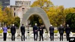 ລັດຖະມົນຕີຕ່າງປະເທດ ສະຫະລັດ ທ່ານ John Kerry, ກາງຊ້າຍ, ໂອບອ້ອມ ລັດຖະມົນຕີຕ່າງປະເທດຂອງຍີ່ປຸ່ນ ທ່ານ Fumio Kishida, ກາງຂວາ, ຫຼັງຈາກທີ່ພວກເພິ່ນ ພ້ອມດ້ວຍຄູ່ຕຳແໜ່ງ ຈາກກຸ່ມປະເທດ G7 ວາງພວງມາລາ ຕໍ່ໜ້າ ສວນອານຸສາວະລີ ສັນຕິພາບ ຮີໂຣຊີມາ ໃນນະຄອນ Hiroshima, ຢູ່ທາງພາກຕາເວັນຕົກ ຂອງຍີ່ປຸ່ນ.