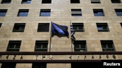 A European Union flag (L) flutters next to a Greek flag on the facade of the Bank of Greece headquarters in Athens, April 14, 2015.