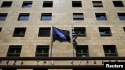 A European Union flag, left, flutters next to a Greek flag on the facade of the Bank of Greece headquarters in Athens, April 14, 2015.