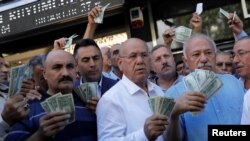 Businessmen holding U.S. dollars stand in front of a currency exchange office in response to the call of Turkish President Tayyip Erdogan on Turks to sell their dollar and euro savings to support the lira, in Ankara, Aug. 14, 2018.