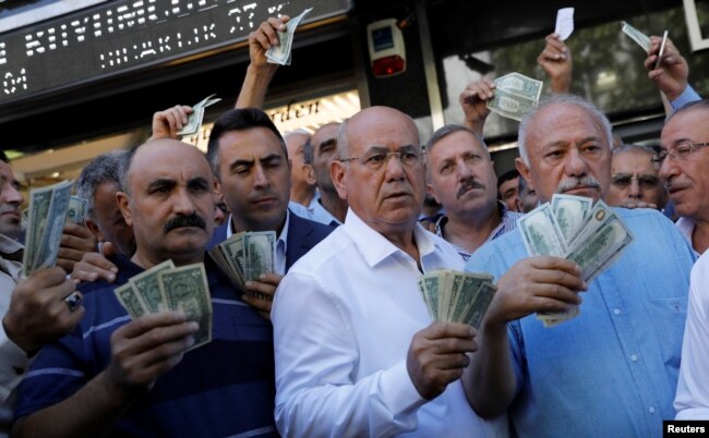 Businessmen holding U.S. dollars stand in front of a currency exchange office in response to the call of Turkish President Tayyip Erdogan on Turks to sell their dollar and euro savings to support the lira, in Ankara, Aug. 14, 2018.