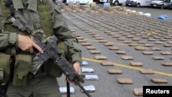 FILE - A Colombian police officer stands guard near packs of marijuana seized in Cali, March 30, 2015. Colombian narcotics police seized 4.1 tons of marijuana from drug trafficking gangs in two houses in Corinto, Cauca, according to authorities. 