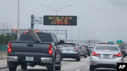 Signs advising drivers to turn on their lights and turn off their flashers while driving in the rain are shown, May 25, 2018, along Interstate 95 near Fort Lauderdale, Fla.