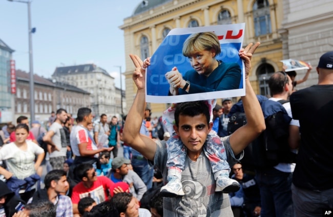 FILE - In this Sept. 4, 2015 file photo a migrant holds up a poster of German Chancellor Angela Merkel before starting a march out of Budapest, Hungary, towards Austria.