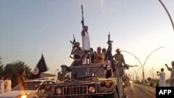 FILE - Fighters from the Islamic State group parade in a commandeered Iraqi security forces vehicle in Mosul, Iraq.