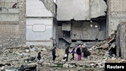 Trẻ em đi trên đống gạch đá đổ nát cạnh tòa nhà bị hư hại trong khu al-Myassar của thành phố Aleppo, Syria 16/2/15