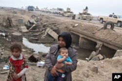 Internally displaced persons stand at a checkpoint as an Iraqi army convoy passes by in Qayyarah, about 31 miles (50 km) south of Mosul, Iraq, Oct. 23, 2016.