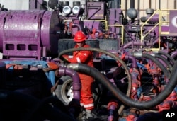 FILE - In this March 25, 2014 file photo, a worker adjusts hoses during a hydraulic fracturing operation at a gas well, near Mead, Colorado.