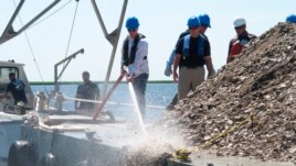 New Jersey Environmental Protection Commissioner Shawn LaTourette, left, uses a high-pressure hose to send clam and oyster shells into the Mullica River in Port Republic, New Jersey, June 29, 2021. (AP Photo)