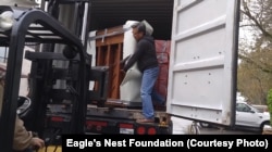 Workers from Eagle's Nest Foundation load pianos donated by Dean Petrich onto a truck to begin their trip to Cambodia.