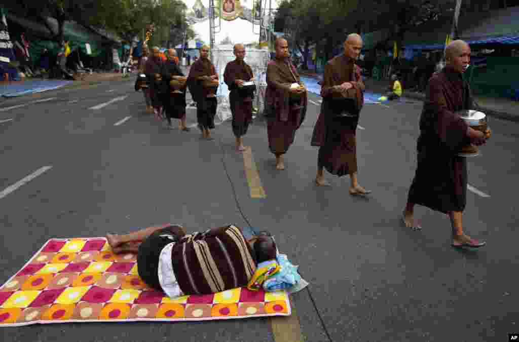 A group of Buddhist monks walk past a sleeping anti-government protester at a protest camp on a road near Government House in Bangkok, Dec. 11, 2013.