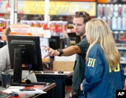 An FBI agent and a detective talk to an employee as they look at a computer screen at an Auto Zone auto parts store, Friday, Oct. 26, 2018, in Plantation, Fla