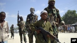 FILE - A young boy leads hard-line Islamist al-Shabab fighters as they conduct military exercises in northern Mogadishu's Suqaholaha neighborhood, Somalia.