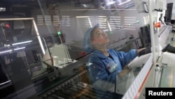 FILE - An employee working on the production line of an electronics factory is seen reflected on an equipment, in Jiaxing, Zhejiang province, China, April 2, 2019.