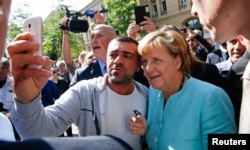 A migrant takes a selfie with German Chancellor Angela Merkel outside a refugee camp near the Federal Office for Migration and Refugees after registration at Berlin's Spandau district, Germany, Sept. 10, 2015.