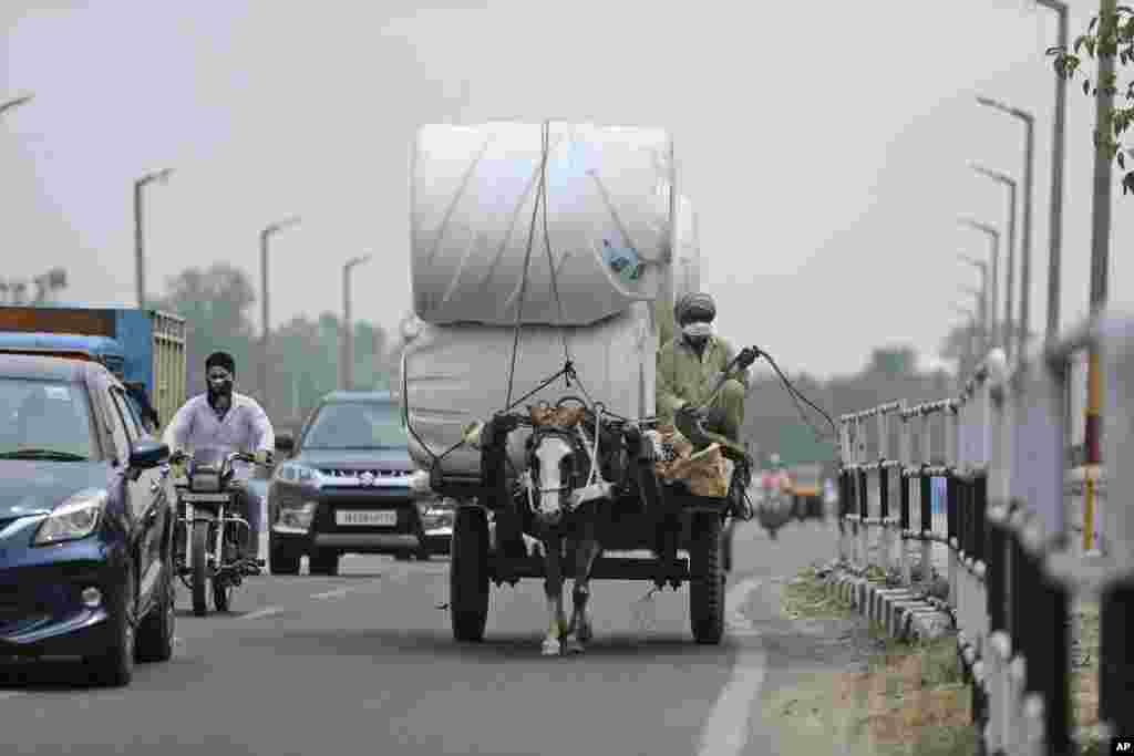 A man wearing a mask rides a horse cart delivering goods in Jammu, India.