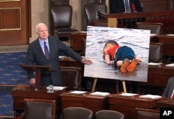 Republican Sen. John McCain displayes a photo of the body of a three year-old Syrian refugee during a speech urging stronger leadership from President Barack Obama on Syria, Sept. 9, 2015.