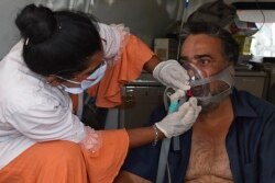 Seorang pasien COVID-19 dengan bantuan oksigen ditolong oleh petugas kesehatan di dalam ambulans sambil menunggu masuk di rumah sakit sipil di Ahmedabad, 3 Mei 2021. (Foto: Sam PANTHAKY / AFP)