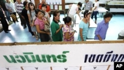 Voters wait in line to cast their votes, next to a board showing information on candidates, at a polling station in Bangkok July 3, 2011.