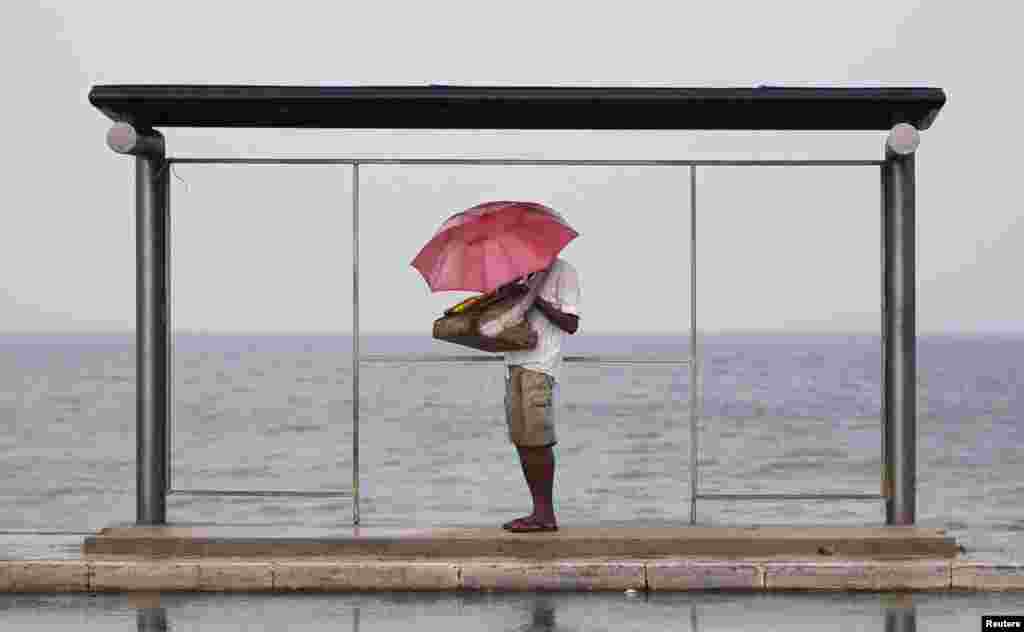 A vendor holds up an umbrella as he seeks shelter from the heavy rain under a bus stand near the Galle Face beach in Colombo, Sri Lanka. 