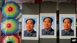 FILE - A salesperson sits near posters of the late communist leader Mao Zedong on display for sale at a shop near Tiananmen Square in Beijing, Sept. 9, 2016.